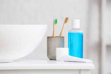 Holder with toothbrushes and products for oral hygiene on table near sink