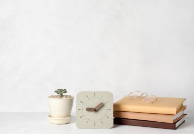 Alarm saati, kitap yığını, gözlük ve ev bitkisi ışık duvarının yanındaki masada.