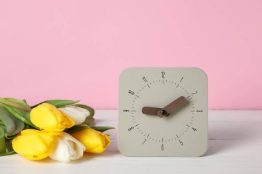 Çalar saat ve lale buketi renk duvarının yanındaki masada.