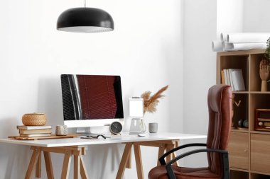 Modern bilgisayar, farklı aletler, çalar saat ve ışık duvarının yanındaki masada kitaplar.