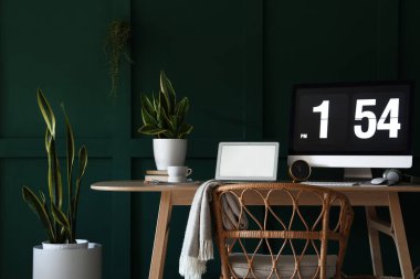 Yeşil duvarın yanında modern bilgisayar, dizüstü bilgisayar ve ev bitkilerine sahip bir işyeri