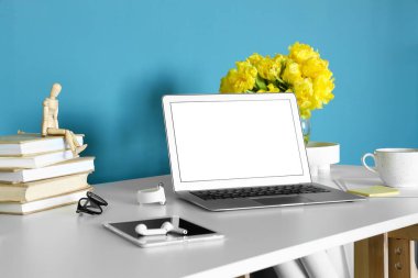 Modern dizüstü bilgisayar, tablet bilgisayar, kulaklık ve akıllı sehpa mavi duvarın yanında.