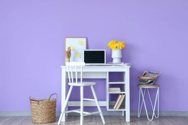 Modern dizüstü bilgisayarı olan bir işyeri ve odanın içindeki renkli duvarın yanında çiçekli vazo.