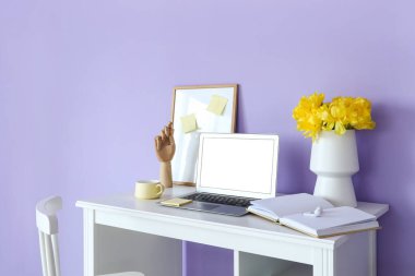 Modern dizüstü bilgisayar, fincan, açık defter ve kulaklıklar renk duvarının yanındaki masada.