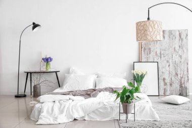 Vazolarda ve lambalarda çiçekler olan aydınlık yatak odasının içinde.