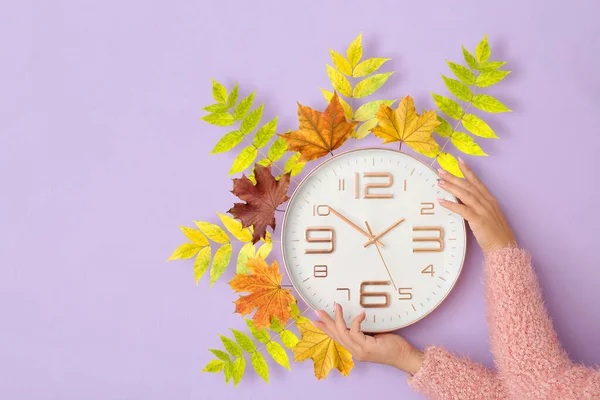 Weibliche Zeiger Mit Uhr Und Herbstblättern Auf Fliederfarbenem Hintergrund Sommerzeit — Stockfoto