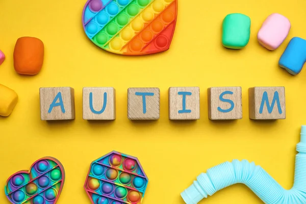 Word AUTISM made of cubes and toys on yellow background