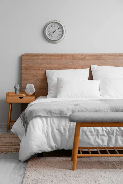 舒适的床 有时尚装饰的床头柜和室内轻墙上的钟 — 图库照片