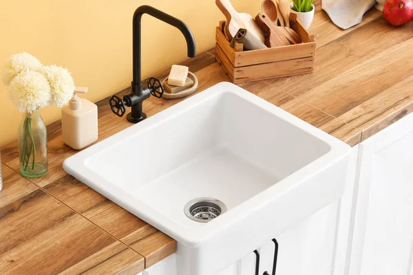 Modern lavabosu olan ahşap tezgah, farklı mutfak aletleri ve renk duvarına yakın kasımpatı çiçekleri.