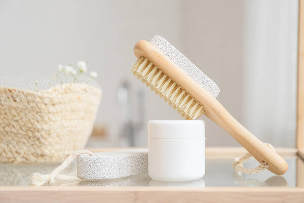 Brush, pumice stones and jar with cosmetic product on shelf in bathroom