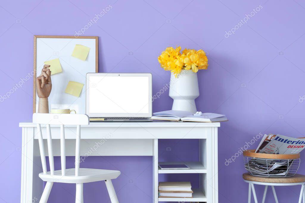 Modern laptop and vase with flowers on table near color wall