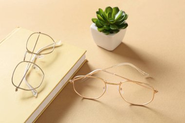 Bej arka planda kitap ve çiçek desenli gözlük, yakın plan.