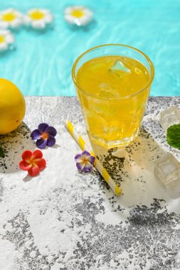 Bir bardak taze limonlu soda ve havuzun kenarında çiçekler.