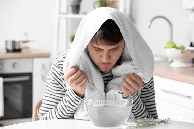 Genç adam burun deliklerini rahatlatmak ve açmak için evde buhar solunumu yapıyor.