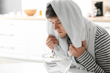 Genç adam burun deliklerini rahatlatmak ve açmak için evde buhar solunumu yapıyor.