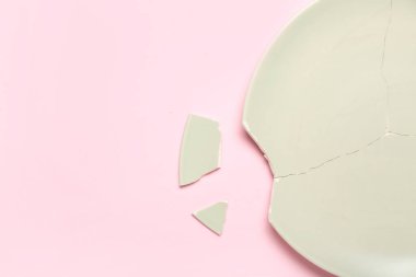 Pembe arka planda kırık seramik plaka, yakın plan.