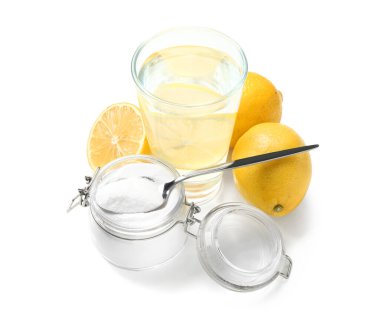 Bir bardak su, kabartma tozu dolu kavanoz ve beyaz arka planda olgun limonlar.