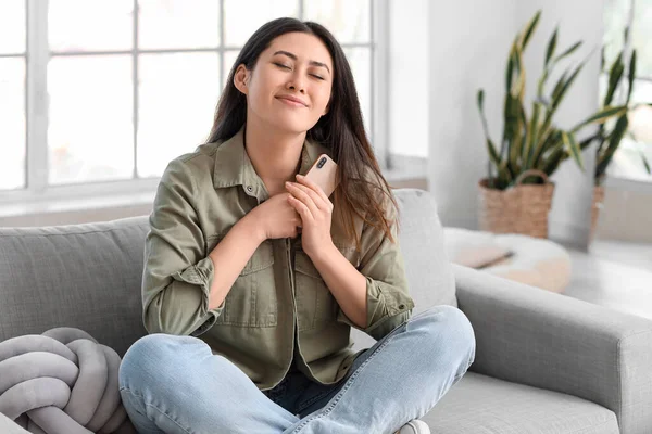 Evdeki kanepede oturan erkek arkadaşından gelen mesajı okuduktan sonra mutlu bir Asyalı kadın.