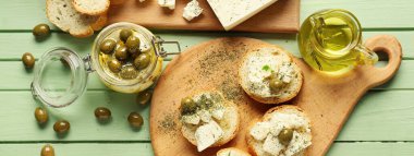 Taze peynirli, zeytinli, baharatlı ve renkli ahşap arka planda bir sürahi yağlı tostlar.