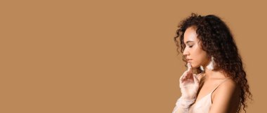 Güzel elbiseli, bej arka planda eldivenleri olan zarif, Afro-Amerikalı bir kadın.