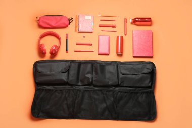 Travel organizer with stationery, headphones and bottles of drink on color background