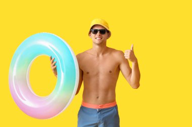 Şişirilebilir yüzüklü çekici genç adam sarı arka planda baş parmak hareketi gösteriyor.