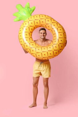 Pembe arka planda şişme yüzüğü olan çekici bir genç adam.