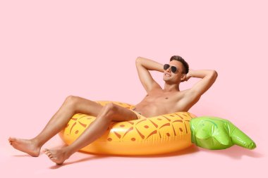 Pembe arka planda şişme yüzüğü olan mutlu genç adam.