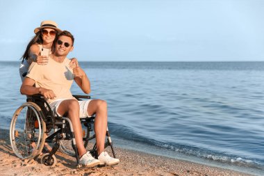 Fiziksel engelli mutlu bir adam ve deniz kenarında selfie çeken kız arkadaşı.