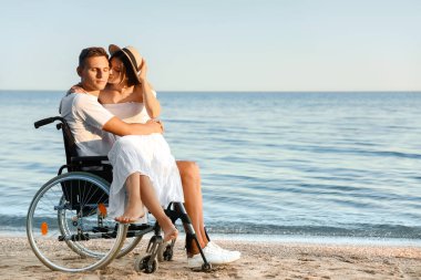Fiziksel engelli mutlu bir adam ve deniz kıyısındaki kız arkadaşı.