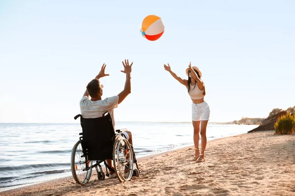 Fiziksel engelli mutlu bir adam ve deniz kenarında top oynayan kız arkadaşı.