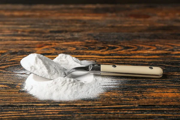 Pile of baking soda and spoon on wooden background