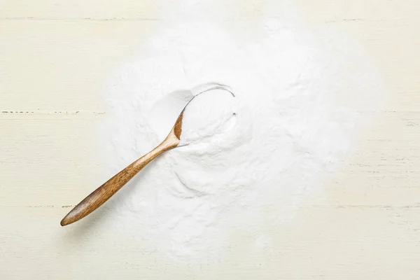Pile of baking soda and spoon on white wooden background