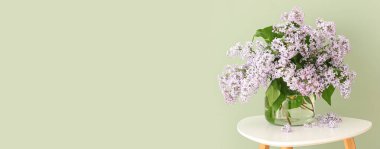 Masanın üzerinde açık yeşil arkaplan ve metin için yeri olan bir demet güzel leylak içeren vazo.