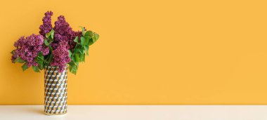 Masanın üzerinde turuncu arkaplan ve metin için yeri olan güzel leylak desenli vazo.