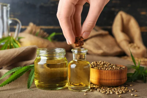 Kenevir yağı şişeleri ve tohumlarla dolu bir kadın eli, yakın plan.