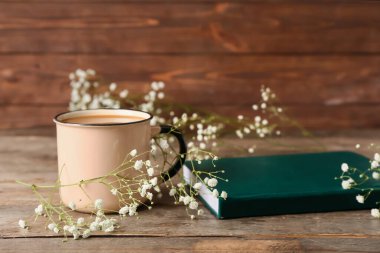 Bir fincan kahve, kitap ve tahta arka planda çingene çiçekleri.