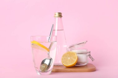 Bir bardak su, kabartma tozu ve limon pembe arka planda.