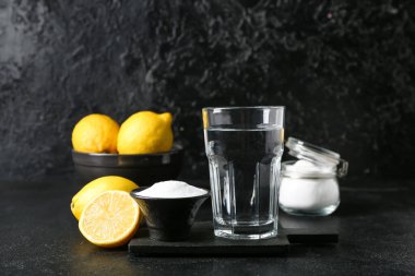 Bir bardak su, kabartma tozu ve koyu arkaplanda olgun limonlar.