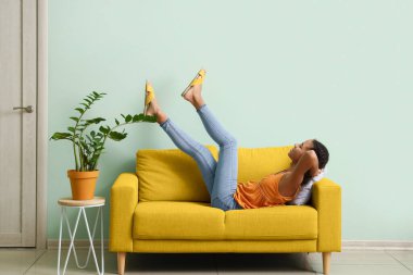 Afro-Amerikalı genç kız oturma odasında kanepede dinleniyor.