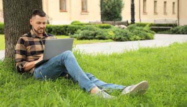 Bilgisayarlı yakışıklı adam yaz parkında dinleniyor.