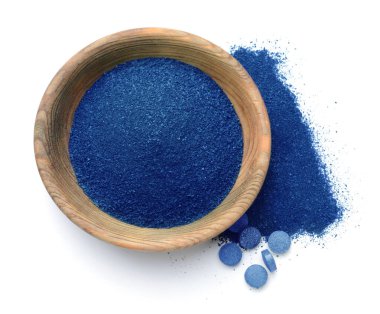 Bowl with blue spirulina powder and pills on white background