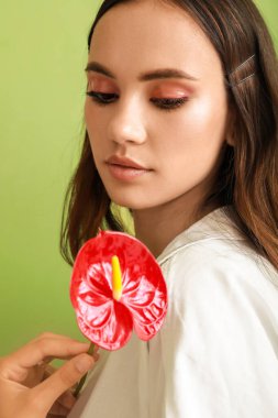 Güzel genç bir kadın yeşil arka planda elinde anthurium çiçeğine bakıyor.