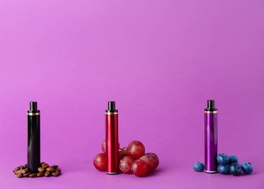 Tek kullanımlık elektronik sigaralar ve mor arka planda farklı meyveler.