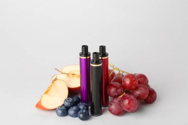 Tek kullanımlık elektronik sigaralar ve arka planda farklı meyveler.