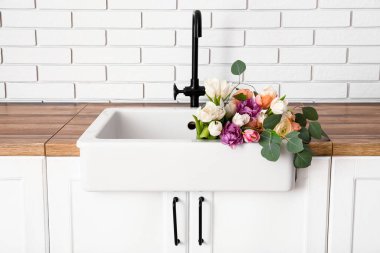 Beyaz tuğla duvarın yanındaki tezgahta güzel çiçeklerle lavabo