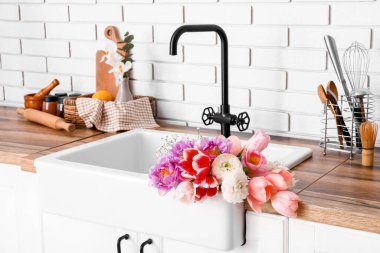 Seramik lavabo, güzel çiçekler ve mutfak gereçleri beyaz tuğla duvarın yanında.