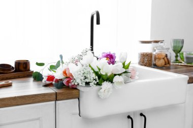 Mutfağın penceresinin yanındaki tezgahta güzel çiçeklerle lavabo.