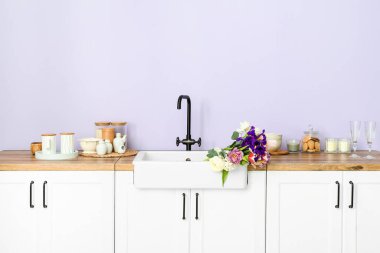 Güzel çiçeklerle lavabo ve mutfak malzemeleri leylak duvarın yanındaki tezgahlarda.