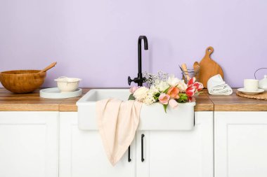 Güzel çiçeklerle lavabo ve mutfak aletleri leylak duvarın yanındaki tezgahlarda.